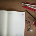 Otvoren planer i pribor za pisanje na drvenom stolu.
